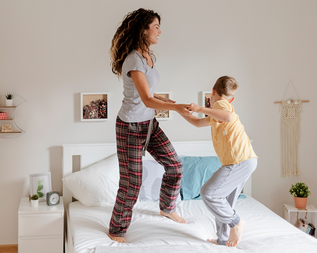 A mother and her young son are jumping on a bed playing in a bright room.