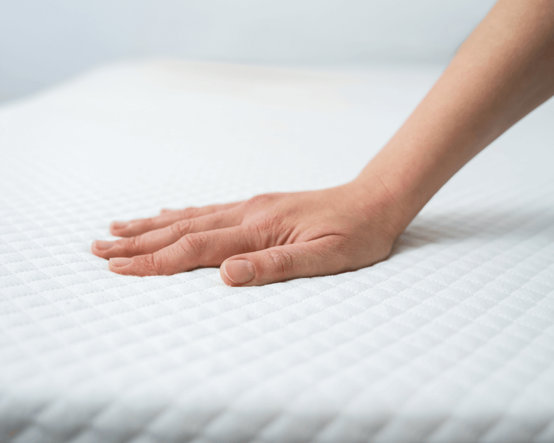 Woman’s hand placed gently on the top of a crisp white mattress.