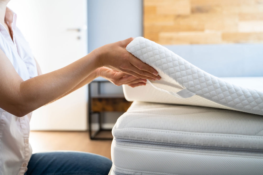 Woman laying a mattress topper onto her mattress in the daylight.