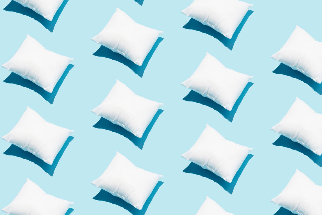 A repeating series of white pillows laying against a baby blue background in the sun.